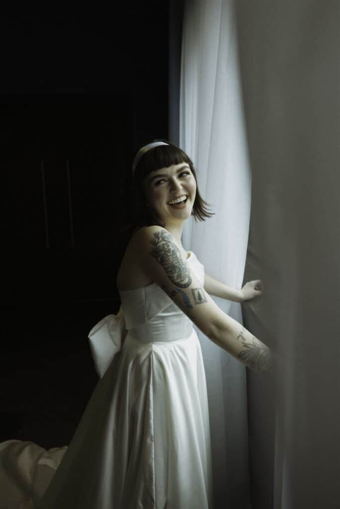 A bride near a window looking over her shoulder laughing