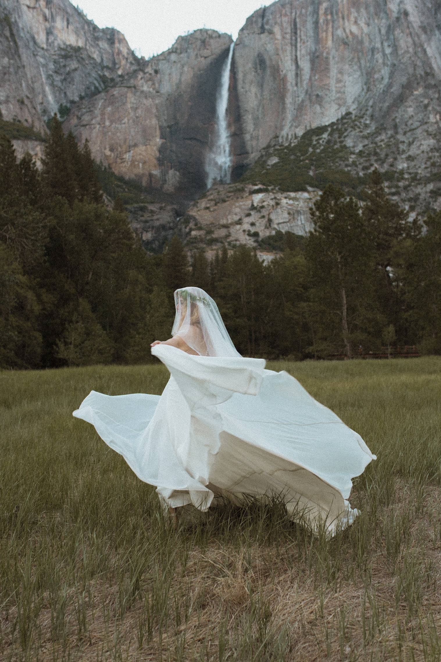 Bride in a flowing white wedding dress running through sunlit meadow during a countryside wedding